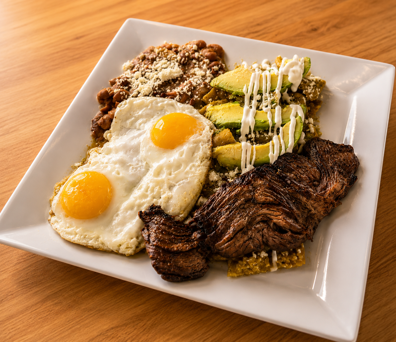 Chilaquiles topped with carne asada, two fried eggs, avocado and refried beans